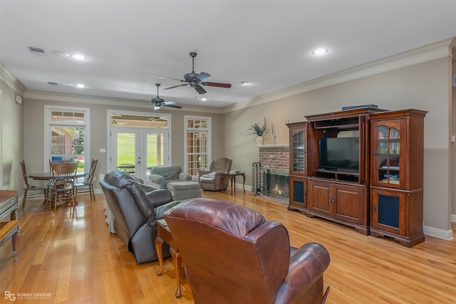 living room with ceiling fan, a brick fireplace, light wood-type flooring, crown molding, and french doors