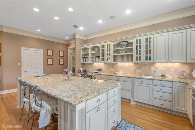 kitchen with light wood-type flooring, a center island, tasteful backsplash, and crown molding