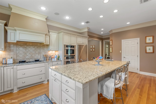 kitchen with light hardwood / wood-style flooring, backsplash, appliances with stainless steel finishes, a kitchen bar, and a kitchen island