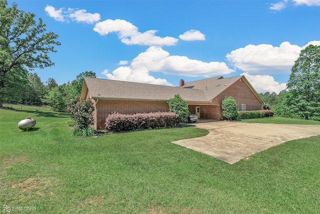 back of house featuring brick siding, a chimney, a lawn, a patio area, and driveway