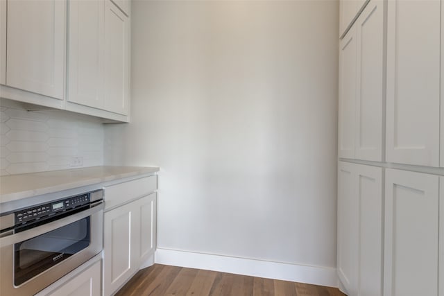 kitchen with light wood-type flooring, stainless steel oven, decorative backsplash, and white cabinets