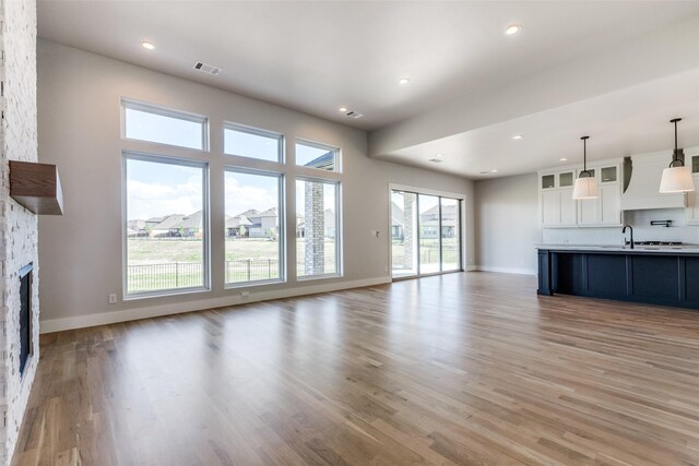 unfurnished living room with plenty of natural light, light hardwood / wood-style flooring, sink, and a stone fireplace