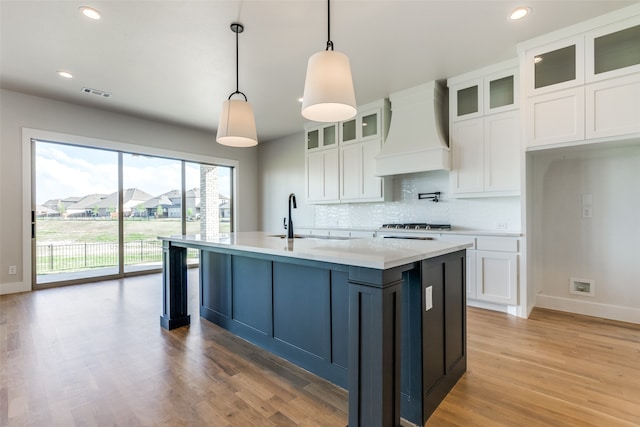 kitchen featuring white cabinets, hanging light fixtures, backsplash, custom exhaust hood, and light hardwood / wood-style floors