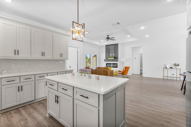 kitchen featuring light wood-style floors, a tray ceiling, a glass covered fireplace, recessed lighting, and backsplash