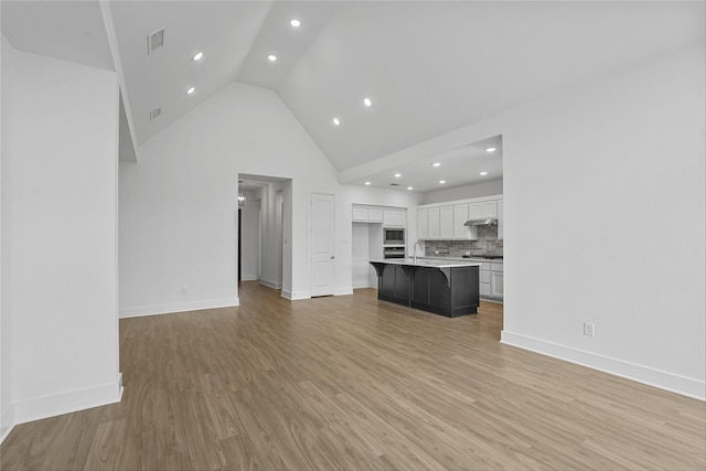 unfurnished living room with sink, light hardwood / wood-style floors, and high vaulted ceiling