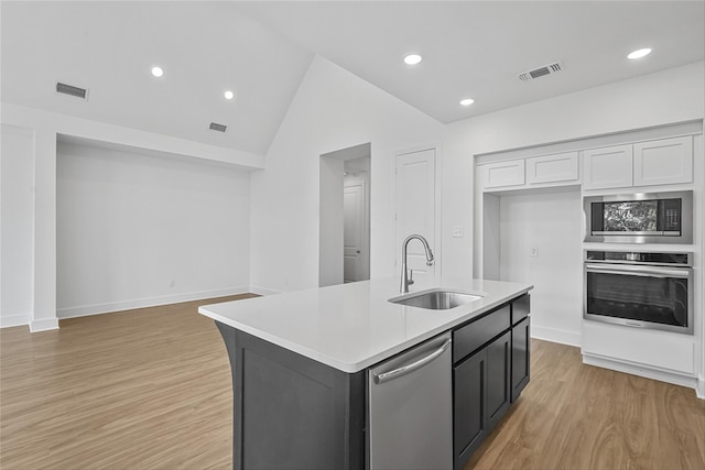 kitchen featuring vaulted ceiling, an island with sink, white cabinets, stainless steel appliances, and sink