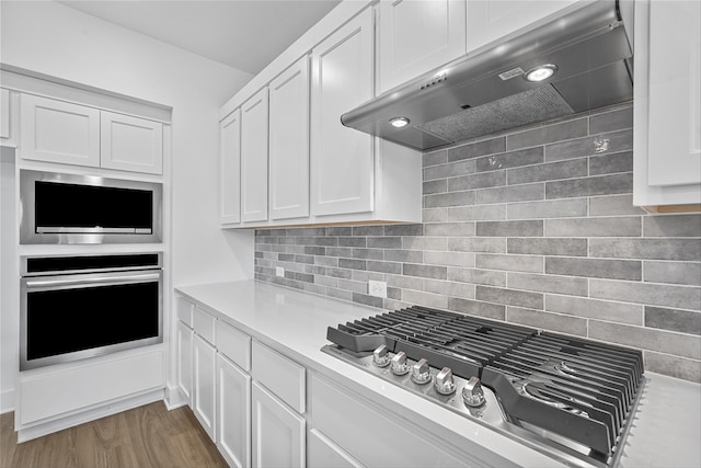 kitchen with white cabinetry, dark wood-type flooring, tasteful backsplash, stainless steel appliances, and exhaust hood