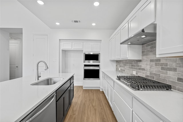 kitchen with white cabinets, stainless steel appliances, light wood-type flooring, range hood, and sink