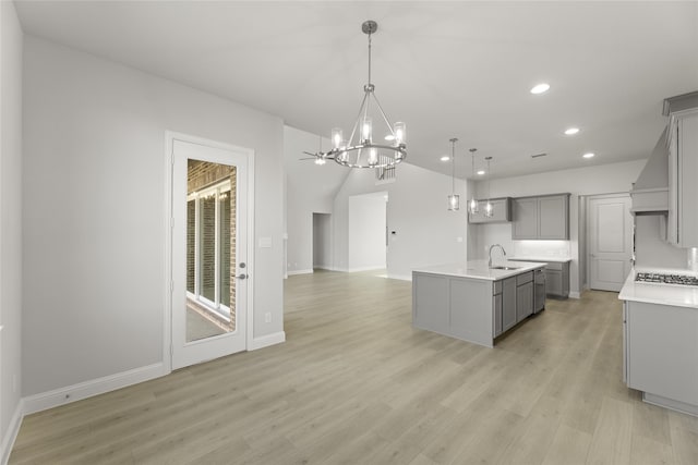 kitchen featuring an inviting chandelier, a kitchen island with sink, light hardwood / wood-style flooring, gray cabinetry, and pendant lighting