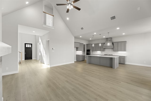 kitchen with gray cabinetry, premium range hood, decorative light fixtures, high vaulted ceiling, and a kitchen island with sink