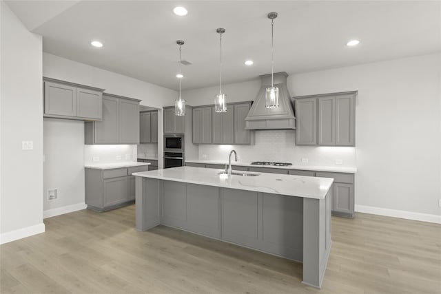 kitchen with custom range hood, a center island with sink, sink, and gray cabinets