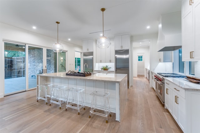 kitchen featuring a spacious island, high quality appliances, pendant lighting, white cabinets, and light hardwood / wood-style floors