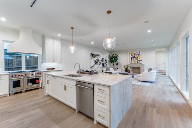 kitchen with sink, stainless steel appliances, custom exhaust hood, white cabinets, and light hardwood / wood-style flooring