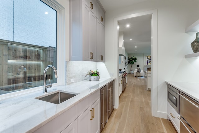 kitchen featuring tasteful backsplash, light stone countertops, sink, light wood-type flooring, and white cabinets