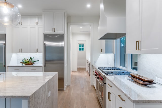 kitchen with light wood-type flooring, decorative light fixtures, white cabinets, light stone counters, and high end appliances