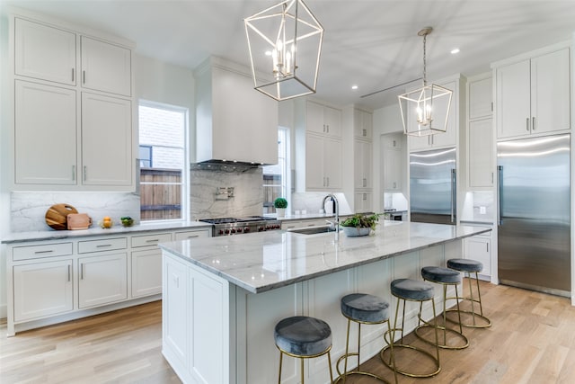 kitchen with a kitchen island with sink, stainless steel built in fridge, sink, and white cabinets