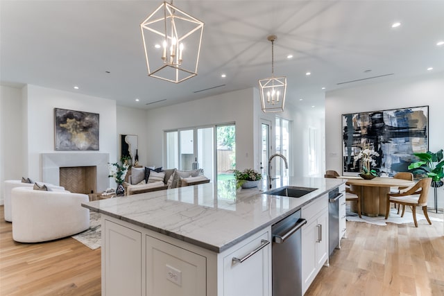 kitchen featuring white cabinetry, sink, a kitchen island with sink, a notable chandelier, and light stone counters