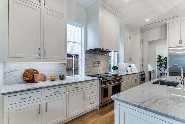 kitchen with wall chimney range hood, sink, backsplash, high quality appliances, and light stone countertops