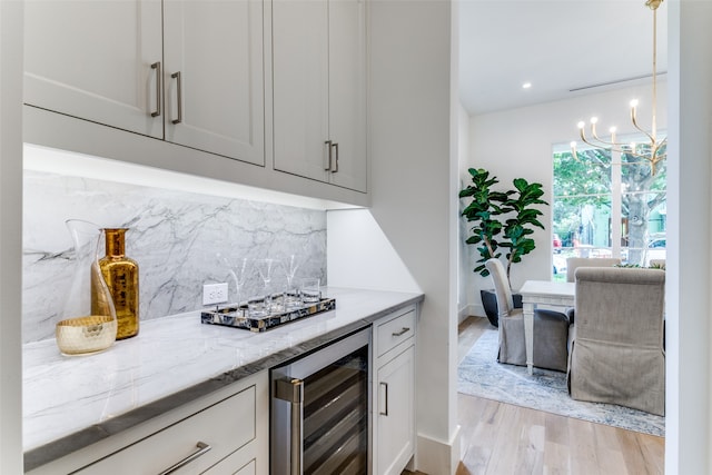 kitchen featuring an inviting chandelier, backsplash, light stone countertops, beverage cooler, and light wood-type flooring