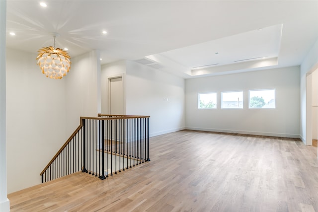 unfurnished room with a raised ceiling, a notable chandelier, and light hardwood / wood-style floors