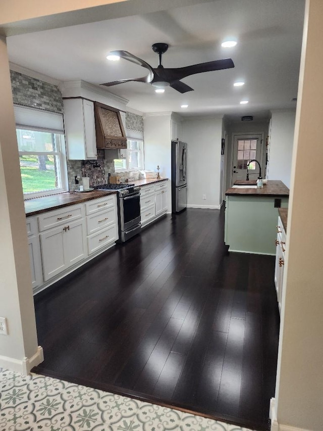 kitchen with premium range hood, appliances with stainless steel finishes, butcher block countertops, white cabinetry, and sink