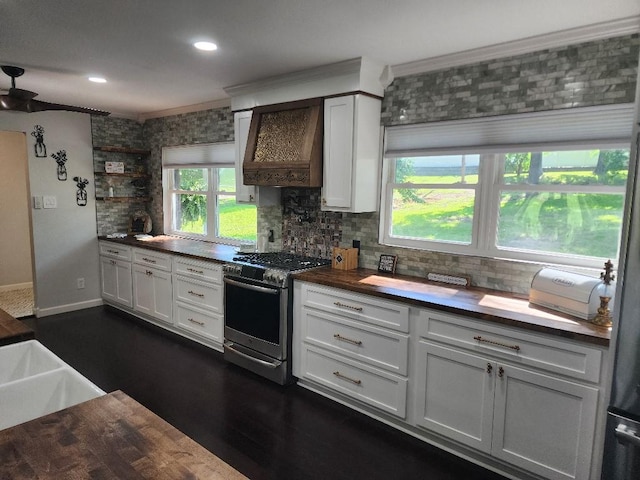 kitchen featuring wood counters, stainless steel gas stove, tasteful backsplash, white cabinets, and custom range hood