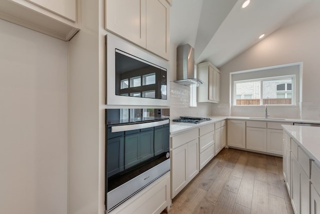 kitchen featuring a sink, wall chimney range hood, tasteful backsplash, appliances with stainless steel finishes, and light countertops