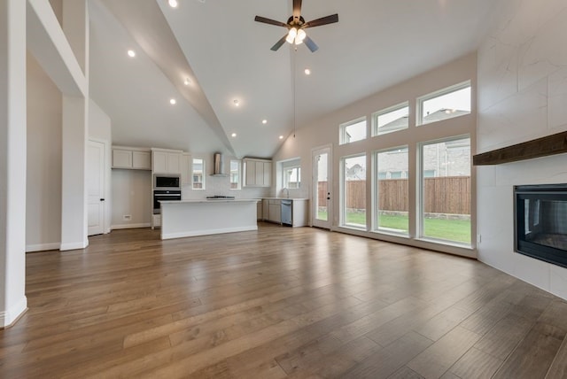 unfurnished living room with hardwood / wood-style floors, ceiling fan, a tile fireplace, and high vaulted ceiling