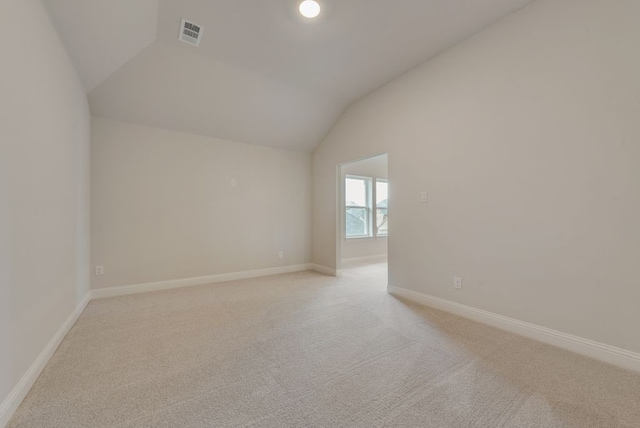 spare room with visible vents, lofted ceiling, light colored carpet, and baseboards