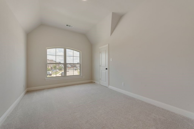 unfurnished room featuring visible vents, light colored carpet, lofted ceiling, and baseboards