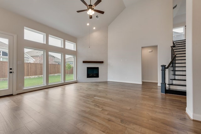 unfurnished living room featuring a fireplace, light hardwood / wood-style flooring, high vaulted ceiling, and ceiling fan