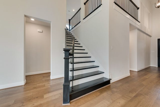 stairs featuring baseboards, wood-type flooring, and a high ceiling