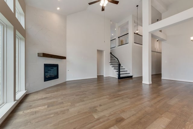 unfurnished living room with wood finished floors, a towering ceiling, a fireplace, ceiling fan, and stairs