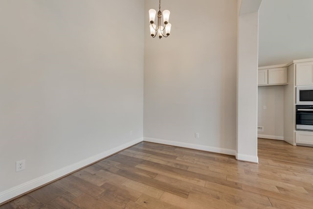 unfurnished dining area featuring light wood finished floors, a notable chandelier, and baseboards