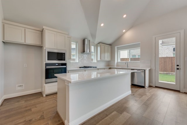 kitchen featuring a kitchen island, wall chimney range hood, light countertops, stainless steel appliances, and a sink