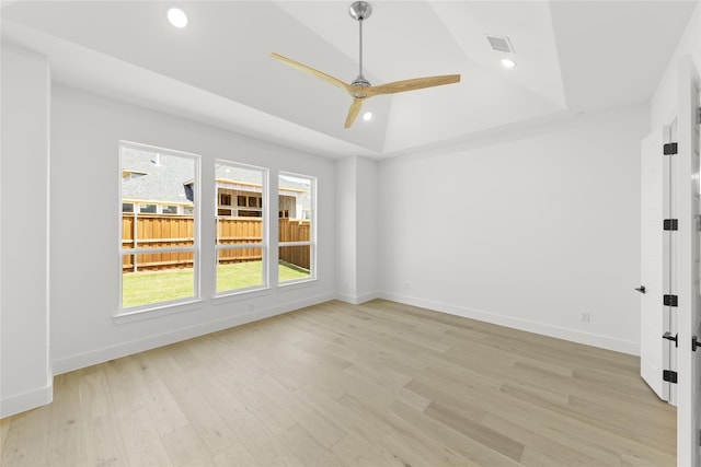 unfurnished room with ceiling fan, vaulted ceiling, a tray ceiling, and light hardwood / wood-style floors