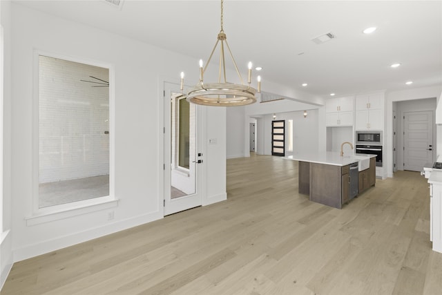 kitchen with a center island with sink, stainless steel microwave, light wood-type flooring, white cabinets, and wall oven