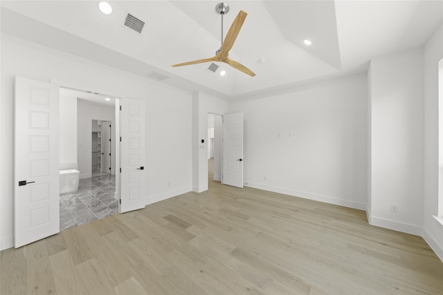 unfurnished bedroom featuring ensuite bath, ceiling fan, a raised ceiling, and light hardwood / wood-style floors