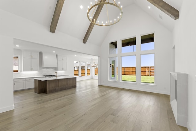 unfurnished living room featuring high vaulted ceiling, a wealth of natural light, light wood-type flooring, beam ceiling, and a chandelier