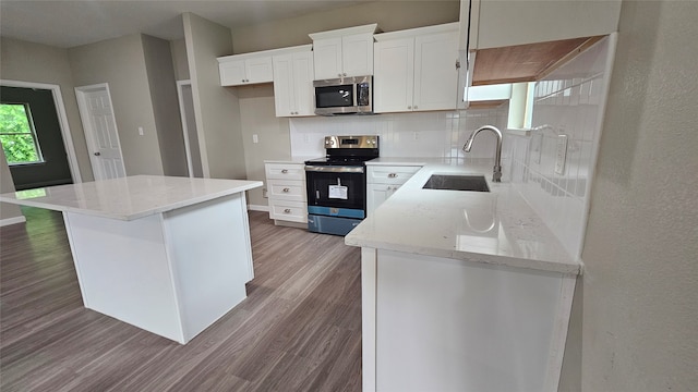 kitchen with white cabinets, backsplash, appliances with stainless steel finishes, sink, and hardwood / wood-style flooring