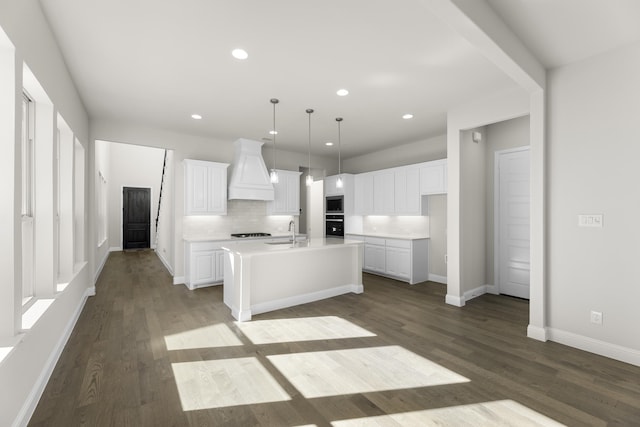 kitchen with white cabinets, wood-type flooring, an island with sink, decorative light fixtures, and custom exhaust hood