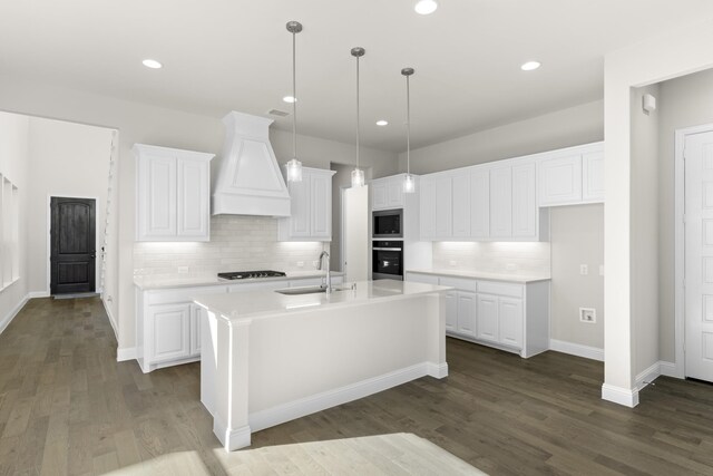 kitchen featuring white cabinetry, stainless steel appliances, dark hardwood / wood-style floors, premium range hood, and a center island with sink