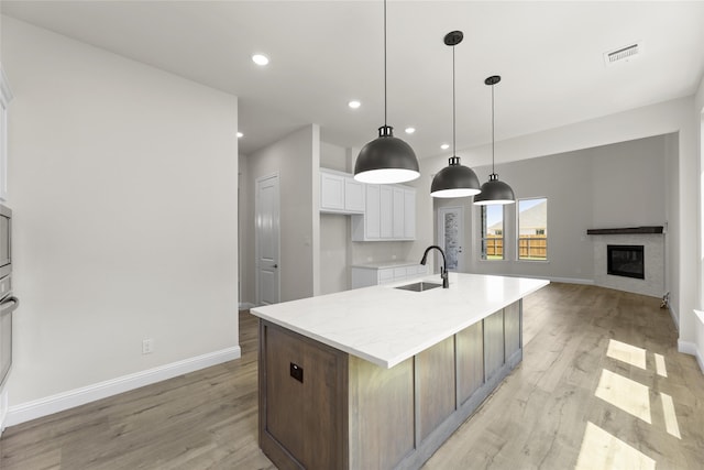 kitchen with sink, an island with sink, decorative light fixtures, white cabinets, and light wood-type flooring