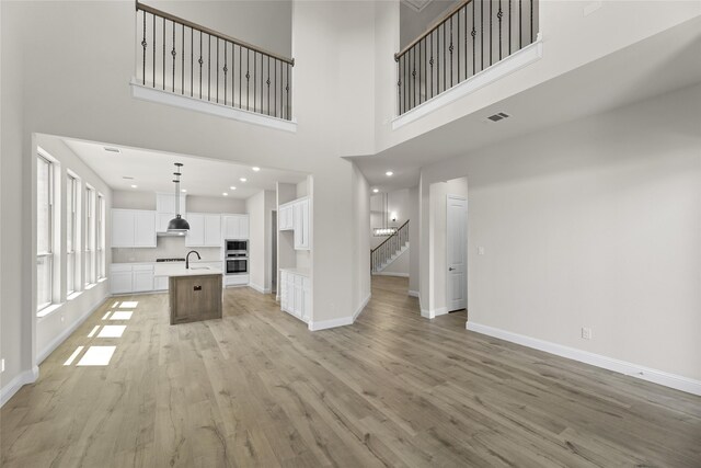 unfurnished living room with light hardwood / wood-style flooring, a towering ceiling, and sink