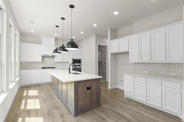 kitchen with a center island with sink, white cabinetry, and hanging light fixtures