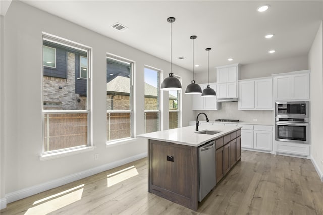 kitchen with white cabinetry, stainless steel appliances, light hardwood / wood-style flooring, decorative light fixtures, and a kitchen island with sink