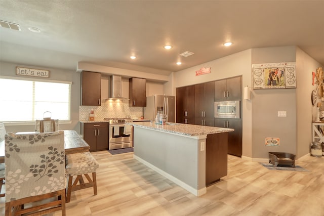 kitchen featuring appliances with stainless steel finishes, light hardwood / wood-style flooring, tasteful backsplash, and wall chimney exhaust hood