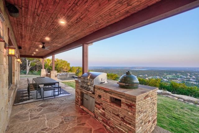 patio terrace at dusk featuring ceiling fan, exterior kitchen, and grilling area