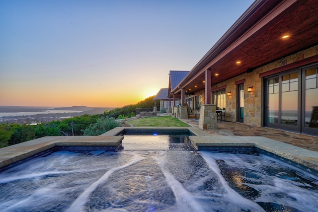 pool at dusk with an in ground hot tub and a patio area