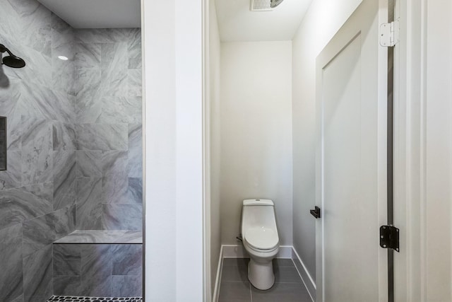 bathroom with toilet, a tile shower, and tile patterned flooring